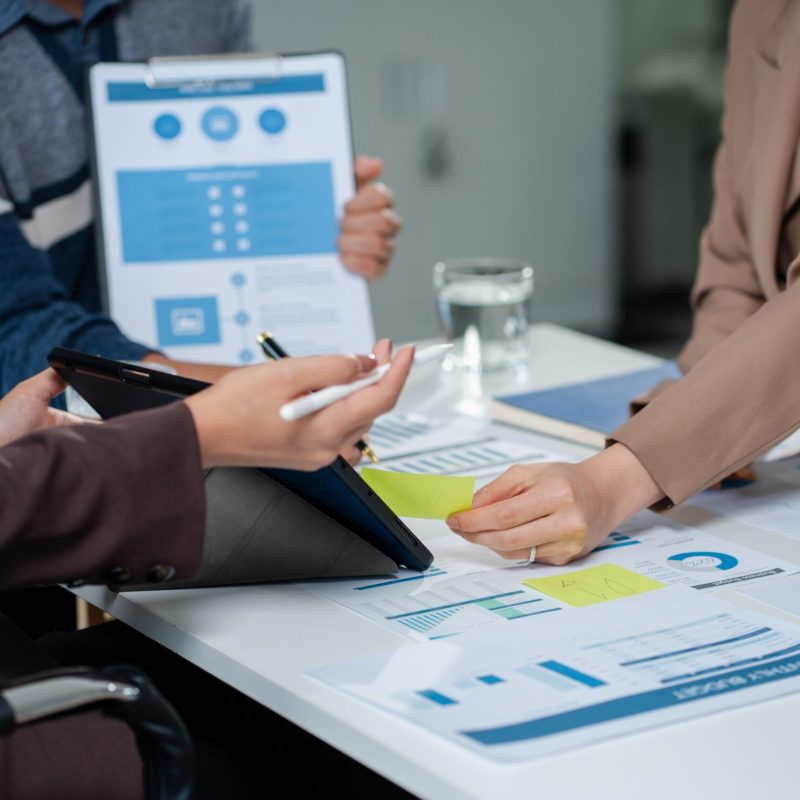 Businessmen write project ideas and use laptops to edit papers for brainstorming sessions with partners in the office.